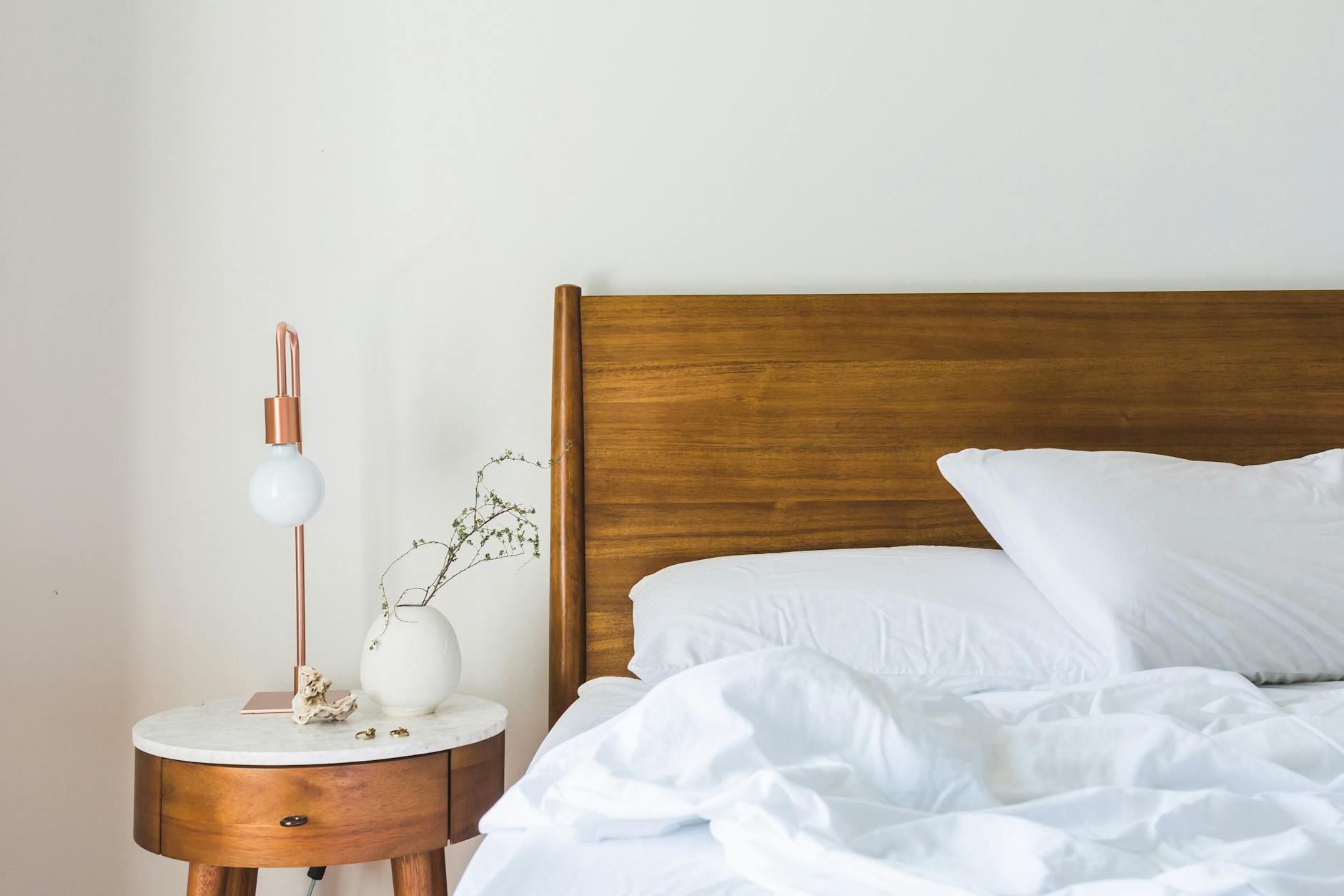 white bedspread beside nightstand with white and copper table lamp