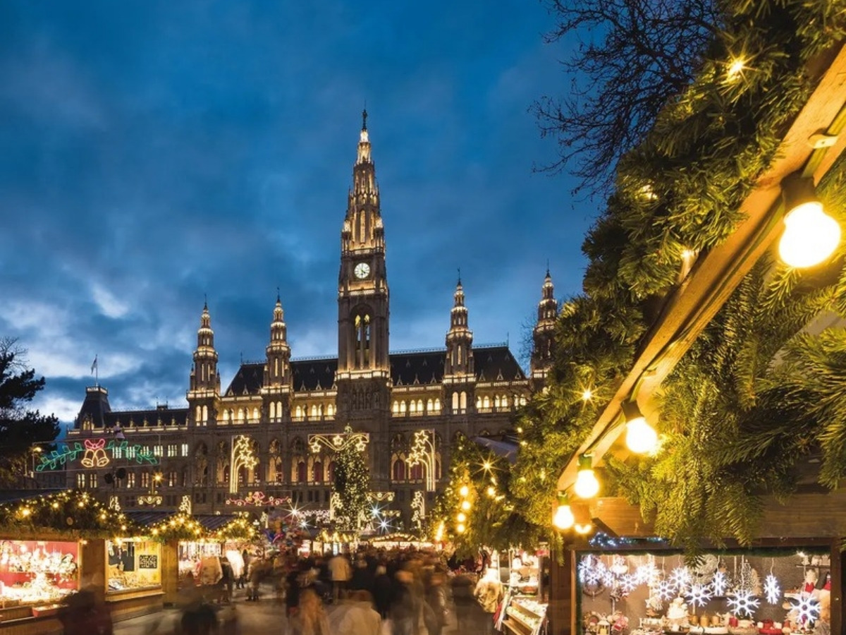The Wiener Christkindlmarkt at dusk, with the illuminated Vienna City Hall rising behind the market stalls